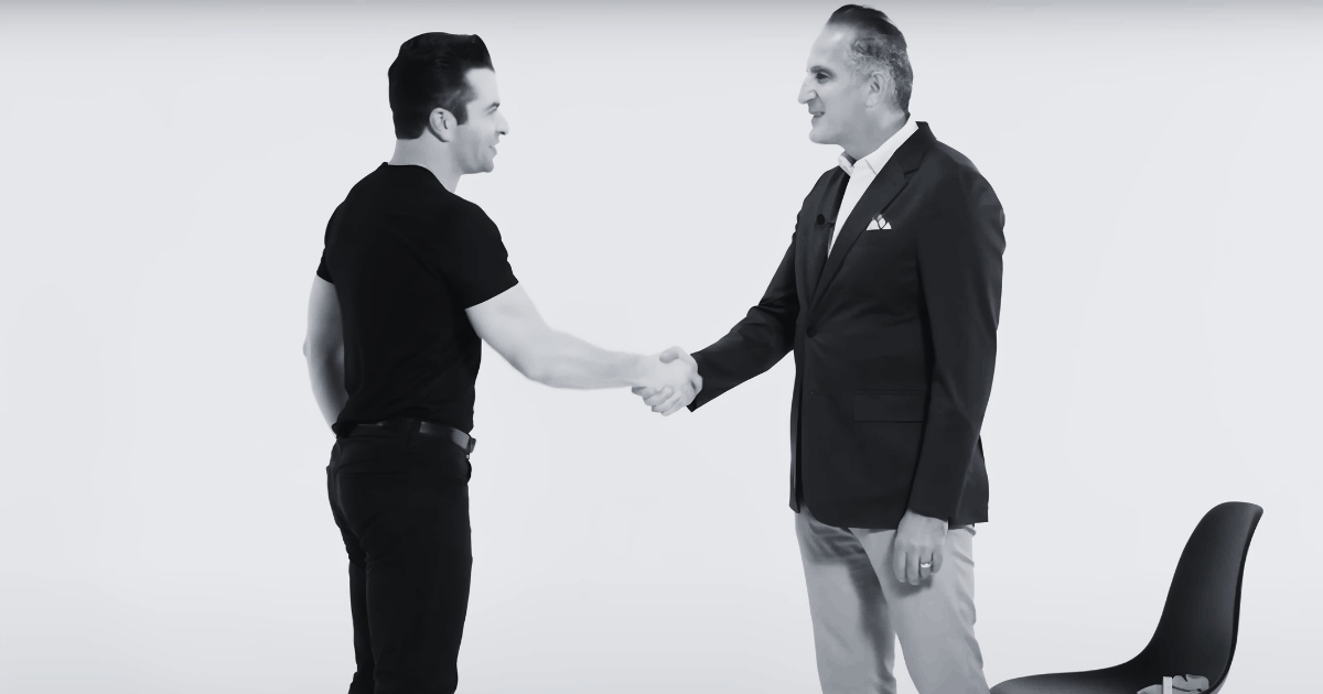 Dr. Taj and his patient smile at each other as they shake hands in a well-lit studio with a white backdrop.
